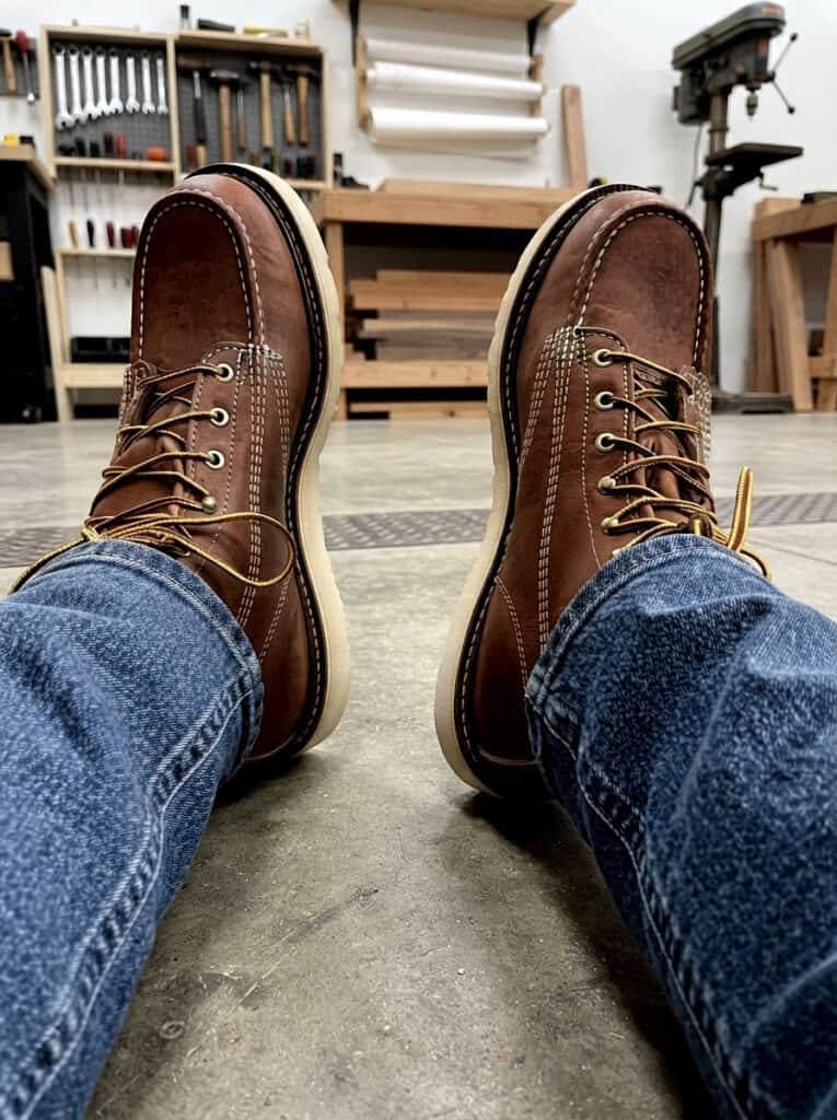 Worn Thorogood American Heritage moc toe boots with creased leather in a woodworking shop