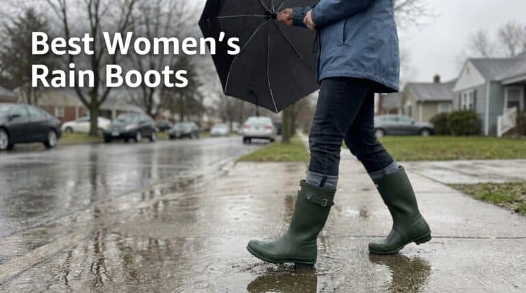 Woman walking in rain with dark green waterproof rain boots on a wet street, holding an umbrella, in a residential neighborhood.