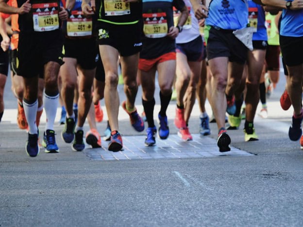 Group of marathon runners with athletic shoes and race bibs during a race event.