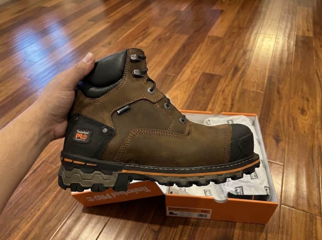 Brown Timberland PRO Boondock 6 inch composite toe boot held above its Timberland PRO box