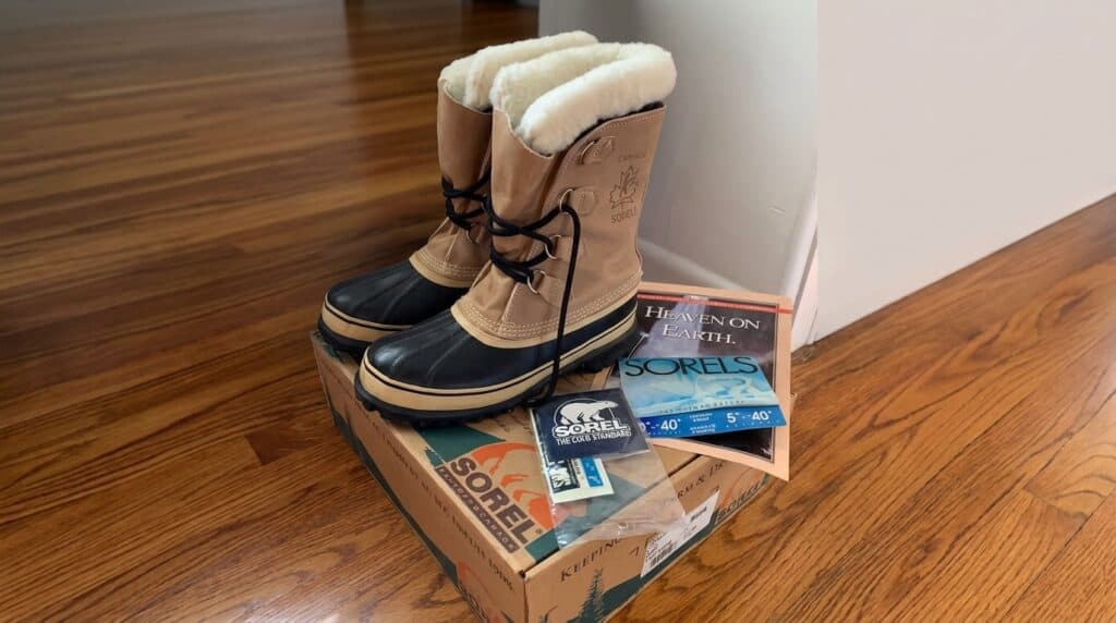Pair of Sorel winter boots with black laces and fur lining, placed on a Sorel shoe box on a wooden floor.