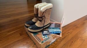 Pair of Sorel winter boots with black laces and fur lining, placed on a Sorel shoe box on a wooden floor.