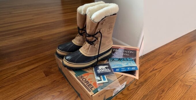 Pair of Sorel winter boots with black laces and fur lining, placed on a Sorel shoe box on a wooden floor.