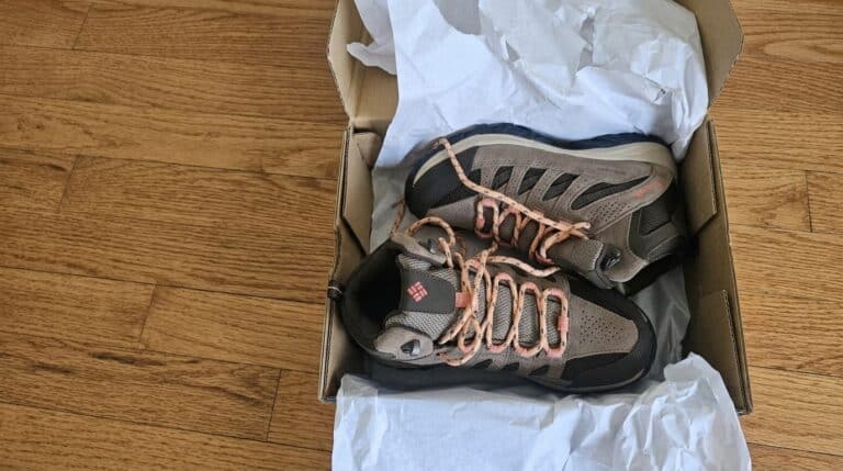 Pair of new hiking shoes in a cardboard box on a wooden floor, ready for outdoor adventures.
