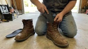 A person kneeling in a garage installing insoles into a pair of rugged work boots for added comfort and support.